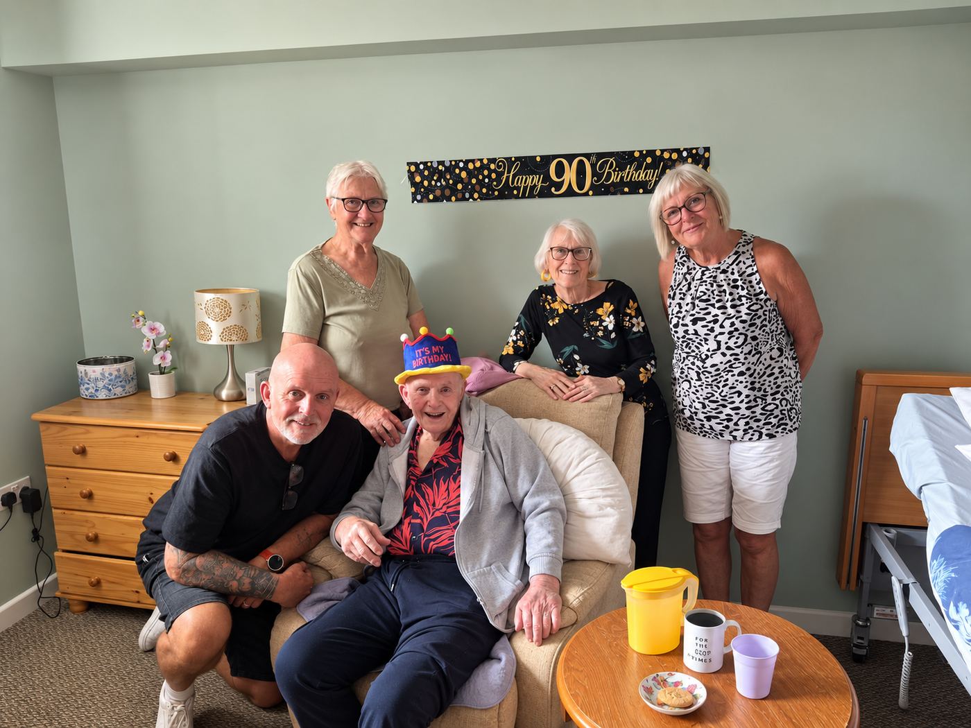 A resident in a party hat celebrating his 90th birthday in his room with his family.