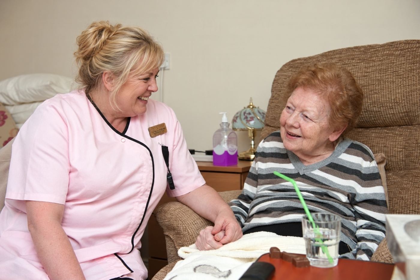 A carer holding a resident&rsquo;s hand as they talk in her room.