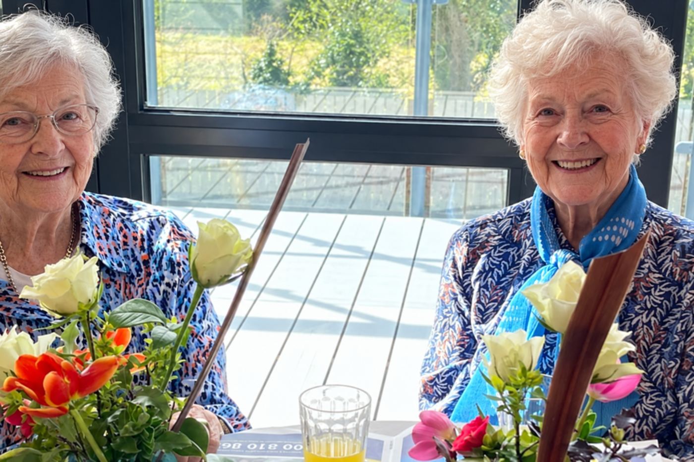 Two residents smiling at a table with a vase of flowers.