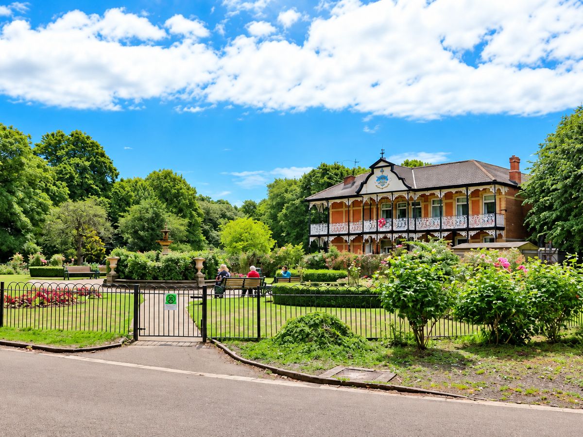Higher Park Lodge from the park path, with the flower beds and fountain of Devonport Park in front of it.