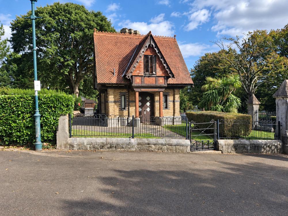 A Victorian gatehouse with a red tiled roof beside the park railings.