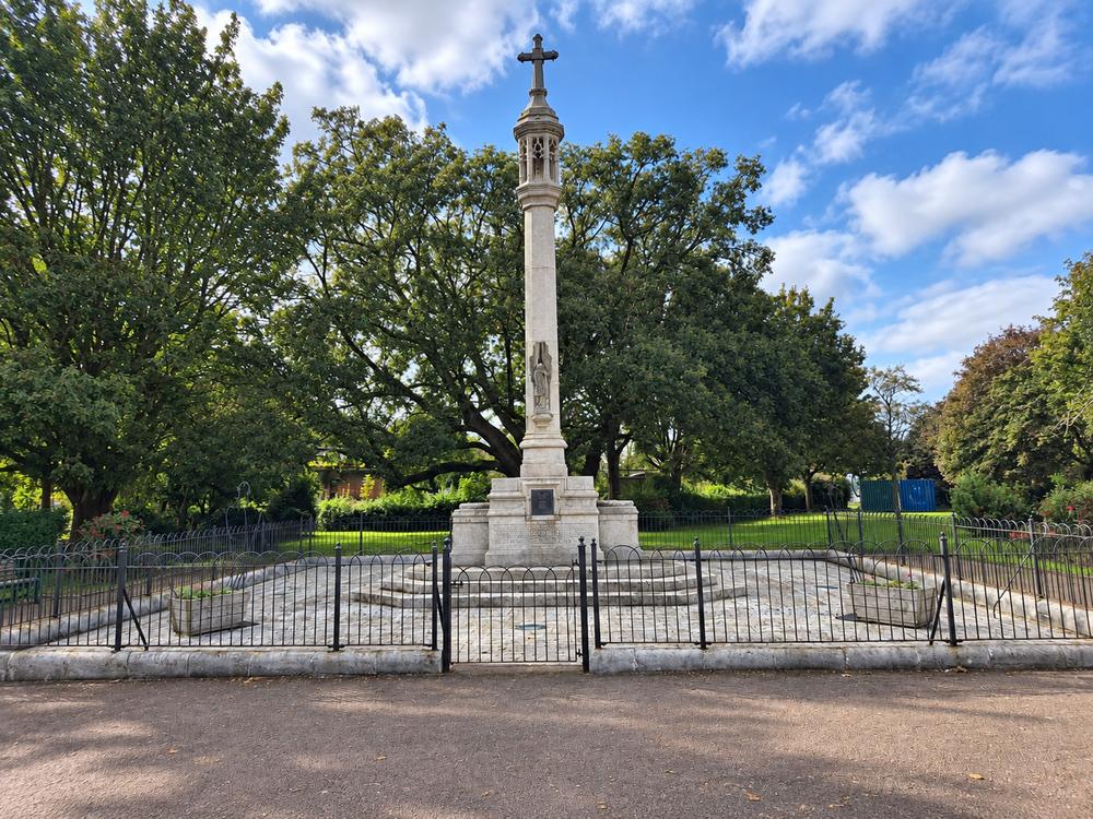 The Great War Memorial, a tall stone column topped with a cross, inside iron railings among the trees.