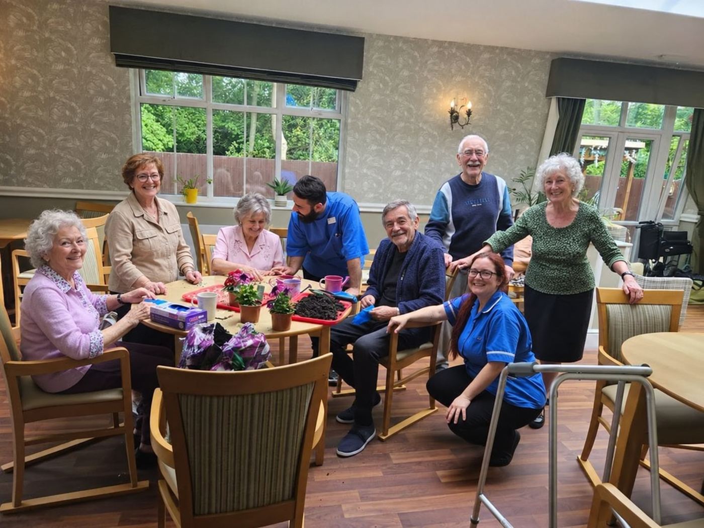 Residents and carers gathered around tables in a bright lounge, smiling.